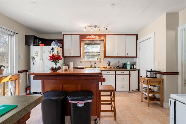 kitchen with a kitchen island, a breakfast bar, freestanding refrigerator, a sink, and decorative backsplash