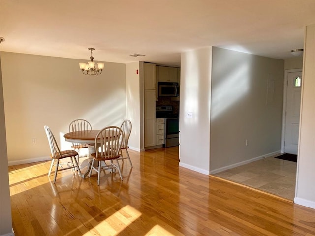 dining space featuring light wood finished floors, a chandelier, and baseboards