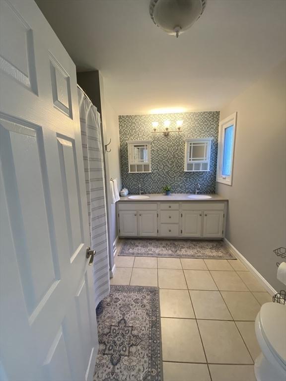 full bathroom with tile patterned floors, toilet, double vanity, baseboards, and a shower with shower curtain