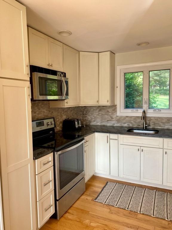 kitchen with stainless steel appliances, a sink, decorative backsplash, light wood-style flooring, and white cabinetry