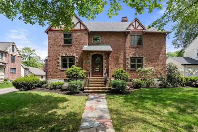english style home featuring a front lawn, brick siding, and a chimney
