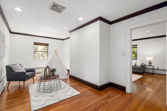 living area with a baseboard heating unit, ornamental molding, plenty of natural light, hardwood / wood-style flooring, and baseboards