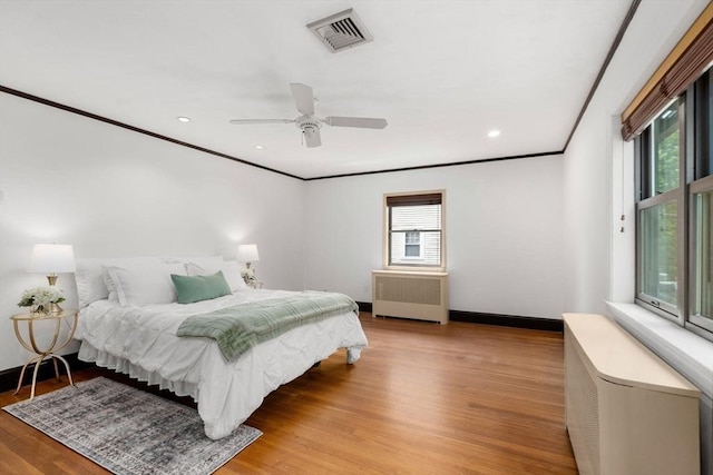 bedroom with radiator, light wood finished floors, ornamental molding, baseboards, and a ceiling fan