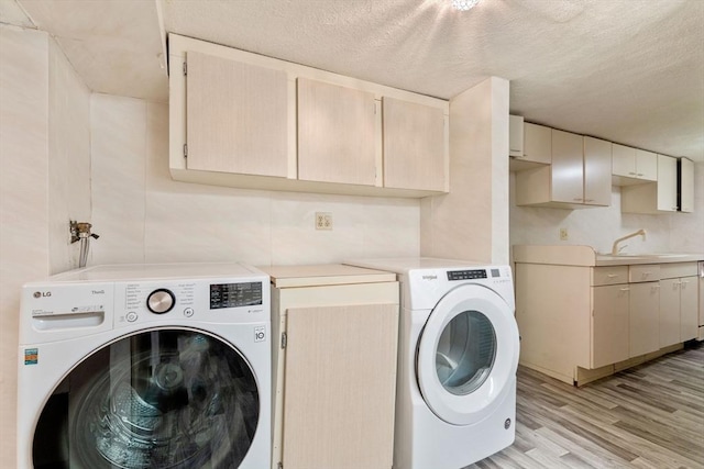 laundry room featuring cabinet space, light wood-style floors, a textured ceiling, and washing machine and clothes dryer