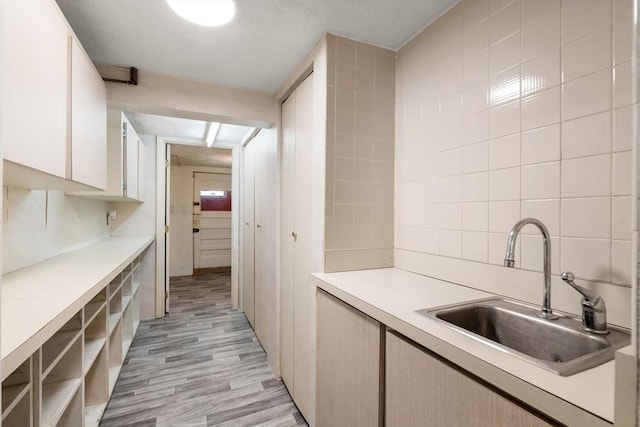 kitchen featuring a sink, light countertops, light wood-type flooring, backsplash, and tile walls