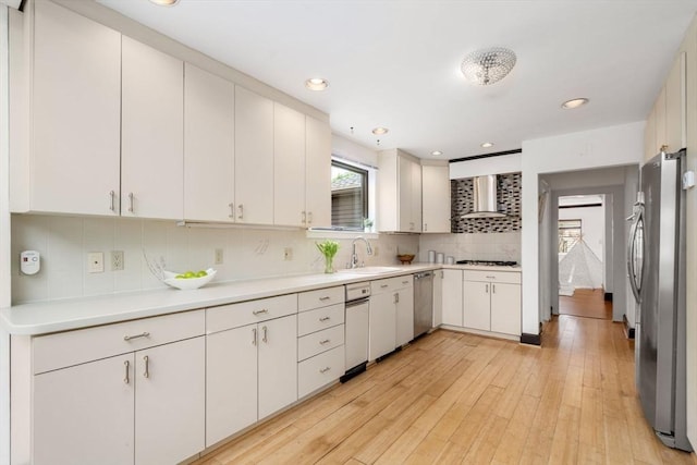 kitchen with stainless steel appliances, wall chimney exhaust hood, a sink, light countertops, and backsplash