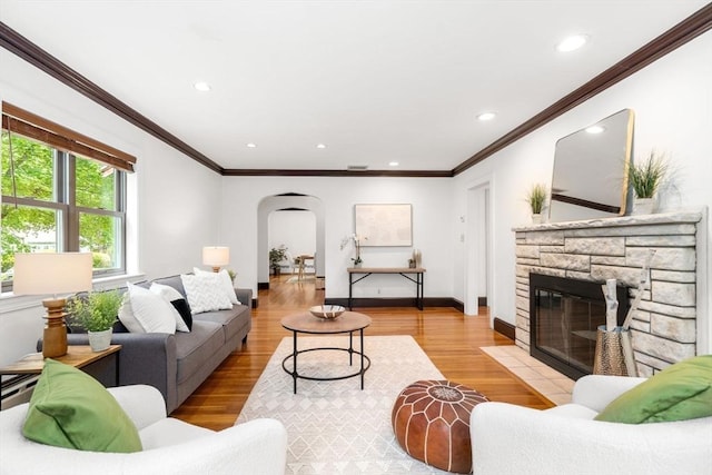 living area featuring arched walkways, crown molding, a stone fireplace, recessed lighting, and light wood finished floors