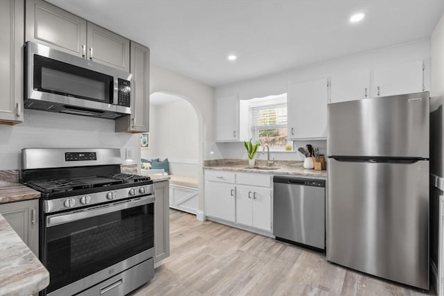 kitchen with appliances with stainless steel finishes, arched walkways, a sink, light wood-style floors, and recessed lighting