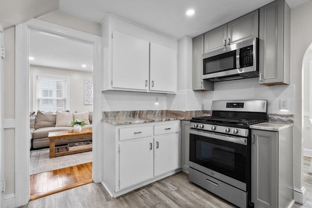 kitchen featuring tasteful backsplash, light stone counters, light wood finished floors, gray cabinetry, and stainless steel appliances