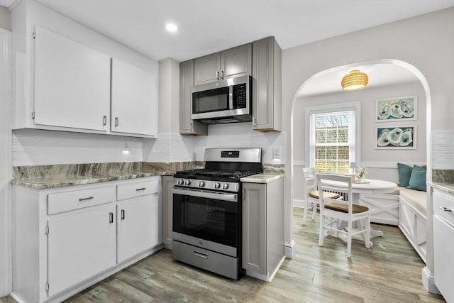 kitchen with arched walkways, light wood-style flooring, gray cabinetry, and stainless steel appliances