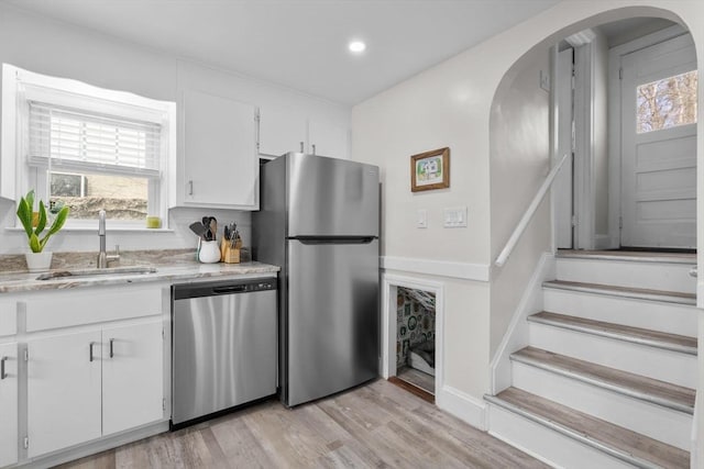 kitchen with appliances with stainless steel finishes, arched walkways, a sink, white cabinets, and light wood-style floors