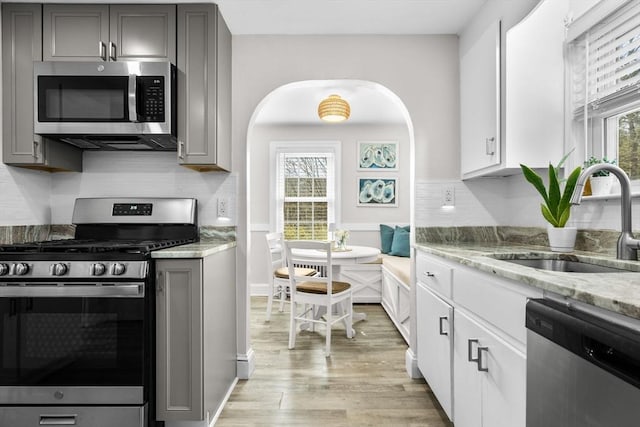kitchen featuring gray cabinets, appliances with stainless steel finishes, light stone countertops, a sink, and light wood-style floors