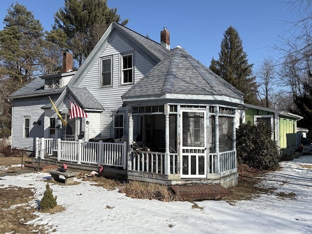 snow covered rear of property featuring a sunroom