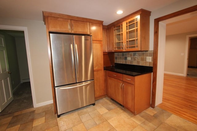 kitchen featuring freestanding refrigerator, glass insert cabinets, decorative backsplash, dark countertops, and baseboards