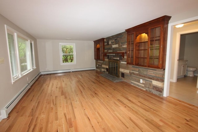 unfurnished living room with light wood-style floors, a stone fireplace, a baseboard radiator, and baseboards