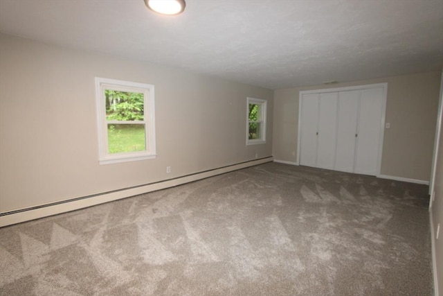 unfurnished bedroom featuring multiple windows, carpet floors, baseboard heating, and a closet