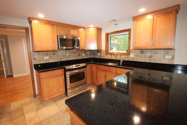 kitchen featuring stainless steel appliances, a sink, dark stone counters, decorative backsplash, and recessed lighting