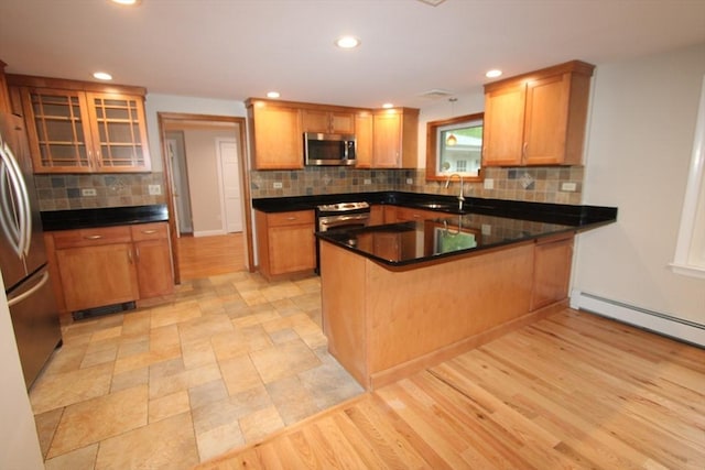 kitchen featuring stainless steel appliances, a peninsula, backsplash, glass insert cabinets, and a sink