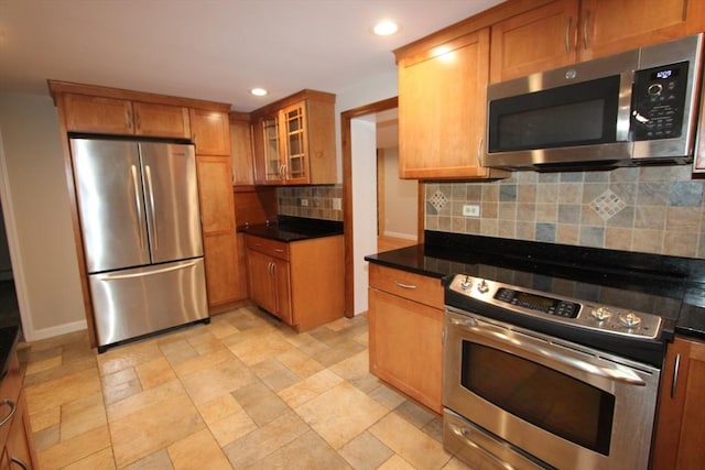 kitchen featuring appliances with stainless steel finishes, tasteful backsplash, brown cabinetry, recessed lighting, and dark countertops
