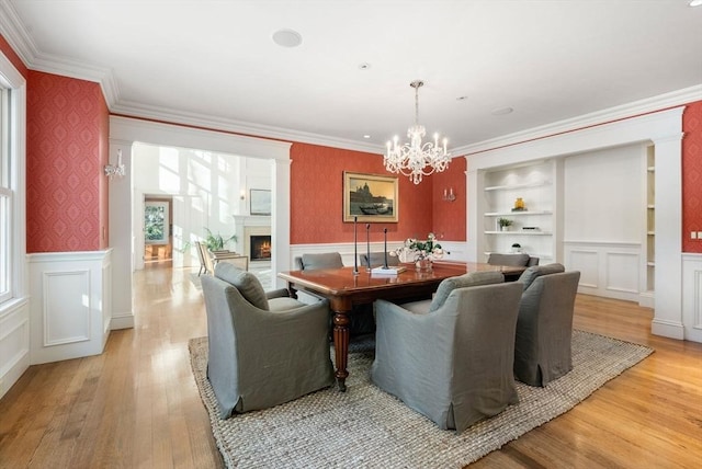 dining space featuring crown molding, a chandelier, built in features, and light hardwood / wood-style flooring