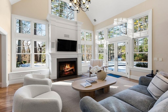 living room featuring a wealth of natural light, high vaulted ceiling, a chandelier, light wood-type flooring, and french doors