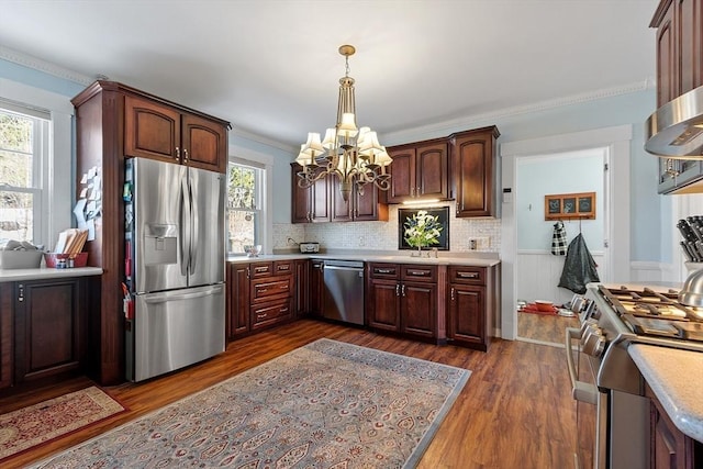 kitchen with appliances with stainless steel finishes, an inviting chandelier, hanging light fixtures, dark hardwood / wood-style flooring, and decorative backsplash