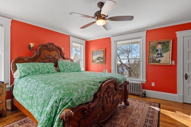 bedroom featuring multiple windows, hardwood / wood-style flooring, radiator heating unit, and ceiling fan