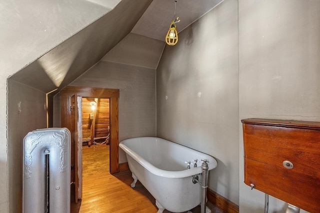 bathroom with hardwood / wood-style flooring, vaulted ceiling, and a tub to relax in