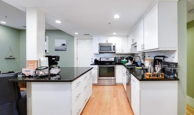 kitchen featuring appliances with stainless steel finishes, a sink, light wood finished floors, decorative backsplash, and white cabinetry