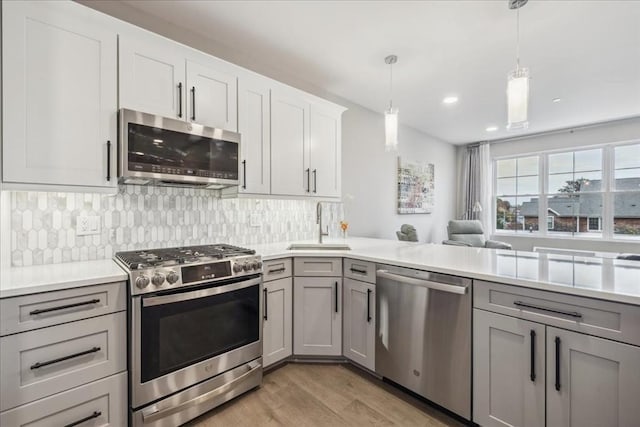 kitchen with sink, gray cabinetry, pendant lighting, stainless steel appliances, and backsplash