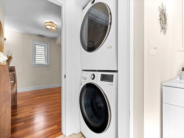 clothes washing area with hardwood / wood-style floors and stacked washer / drying machine