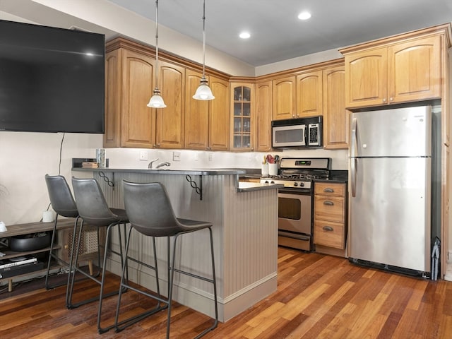 kitchen featuring stainless steel appliances, pendant lighting, dark hardwood / wood-style flooring, and a kitchen breakfast bar