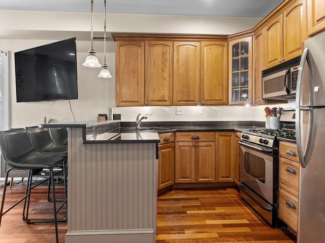 kitchen featuring hanging light fixtures, sink, appliances with stainless steel finishes, a breakfast bar, and dark hardwood / wood-style flooring