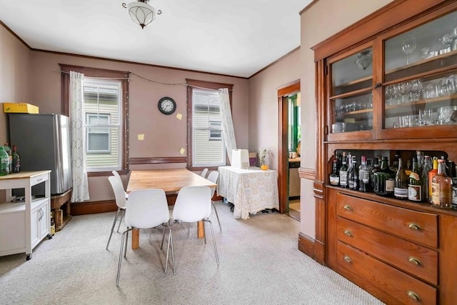 dining space with baseboards, ornamental molding, and light carpet