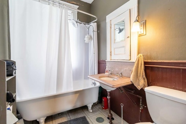 bathroom with a textured wall, wainscoting, toilet, and shower / tub combo
