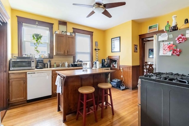 kitchen with appliances with stainless steel finishes, wainscoting, light wood finished floors, a center island, and a ceiling fan