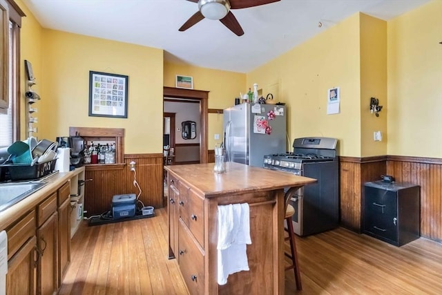 kitchen featuring ceiling fan, a center island, light wood-type flooring, a wainscoted wall, and stainless steel appliances