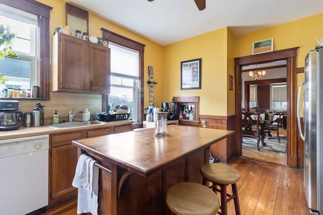kitchen with wainscoting, a sink, light wood finished floors, dishwasher, and freestanding refrigerator