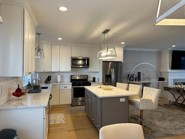 kitchen with appliances with stainless steel finishes, light wood-type flooring, a center island, white cabinetry, and decorative light fixtures