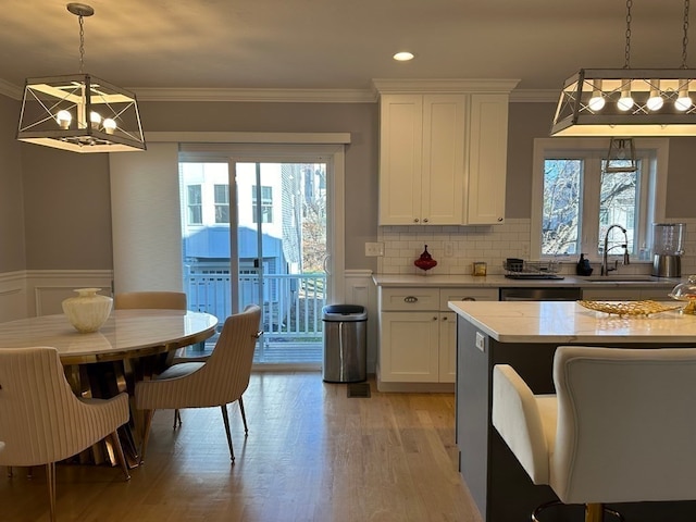 kitchen featuring light wood-type flooring, white cabinetry, decorative light fixtures, and a healthy amount of sunlight