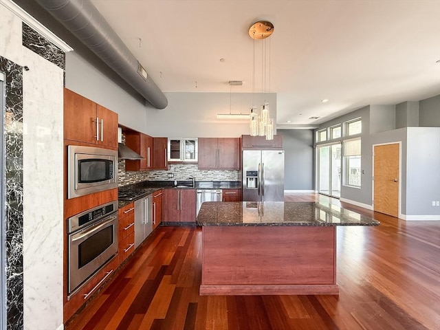 kitchen with appliances with stainless steel finishes, a kitchen island, backsplash, and dark wood-type flooring