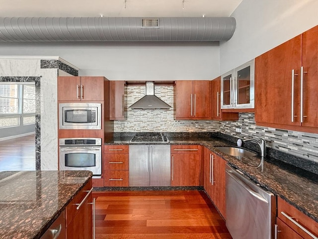kitchen with wall chimney range hood, decorative backsplash, dark wood-style flooring, appliances with stainless steel finishes, and a sink