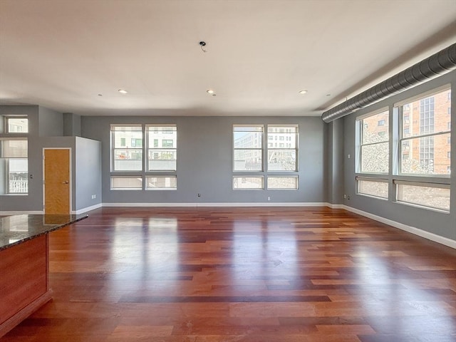 unfurnished living room with baseboards, wood finished floors, and a wealth of natural light