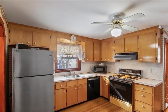 kitchen featuring light countertops, a sink, light wood-type flooring, under cabinet range hood, and black appliances