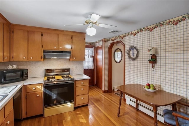 kitchen with light wood finished floors, light countertops, gas range, black microwave, and under cabinet range hood