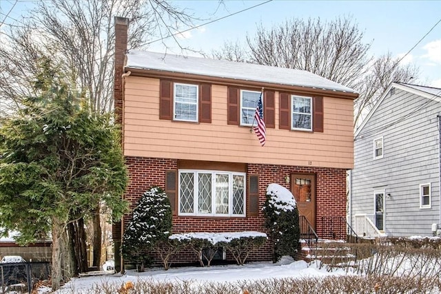 colonial home featuring entry steps, a chimney, fence, and brick siding