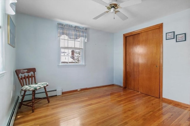 bedroom featuring a closet, baseboard heating, a ceiling fan, wood finished floors, and baseboards