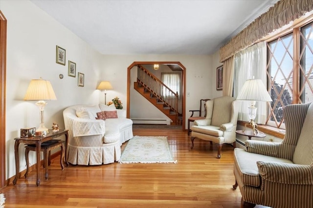 sitting room featuring arched walkways, a baseboard heating unit, wood finished floors, baseboards, and stairs