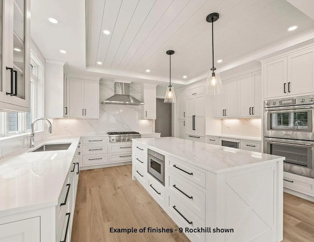 kitchen with a raised ceiling, wall chimney exhaust hood, appliances with stainless steel finishes, light wood-type flooring, and white cabinetry