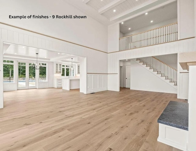 unfurnished living room featuring stairway, beamed ceiling, a towering ceiling, and light wood-style floors